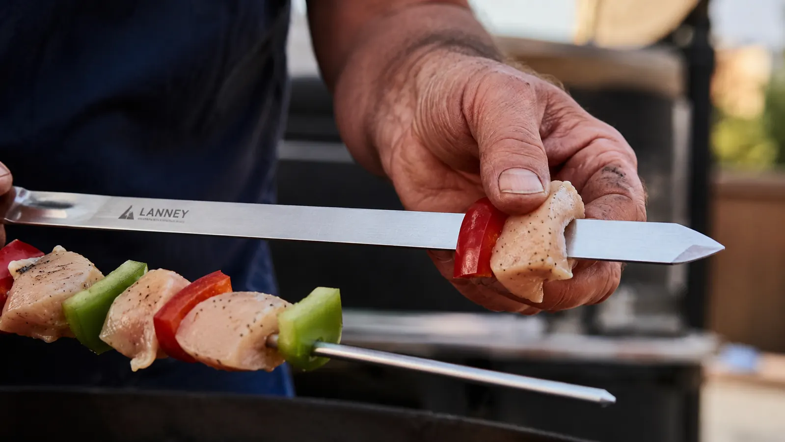 Hand threading chicken and vegetables onto a flat LANNEY skewer over a cutting board