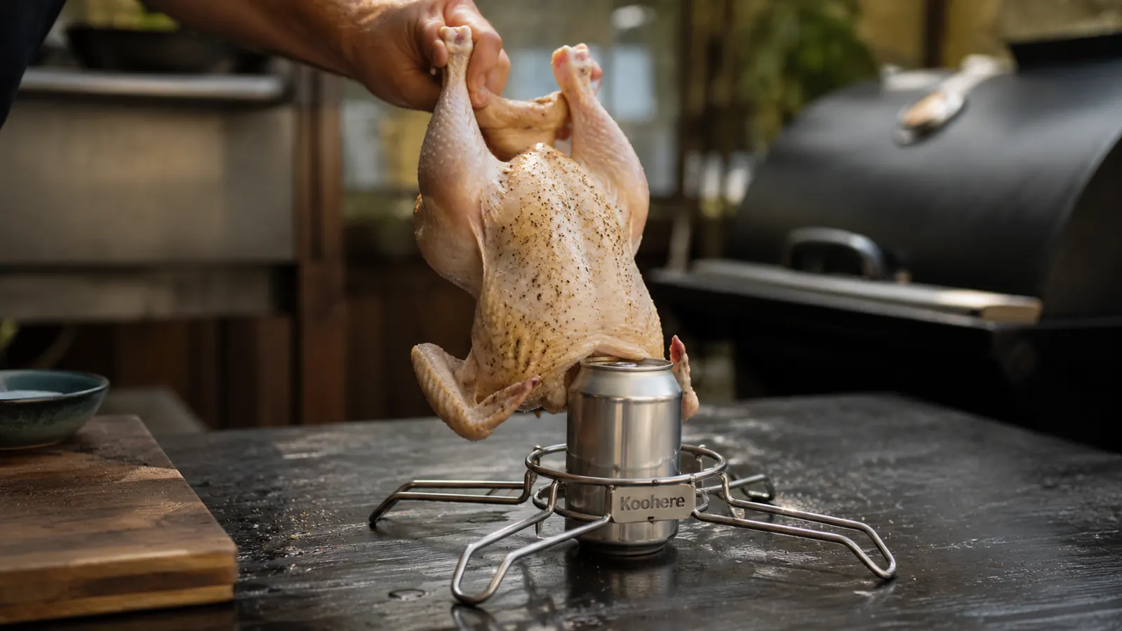 Hand lowering a seasoned whole chicken onto the Koohere stainless steel beer can chicken holder