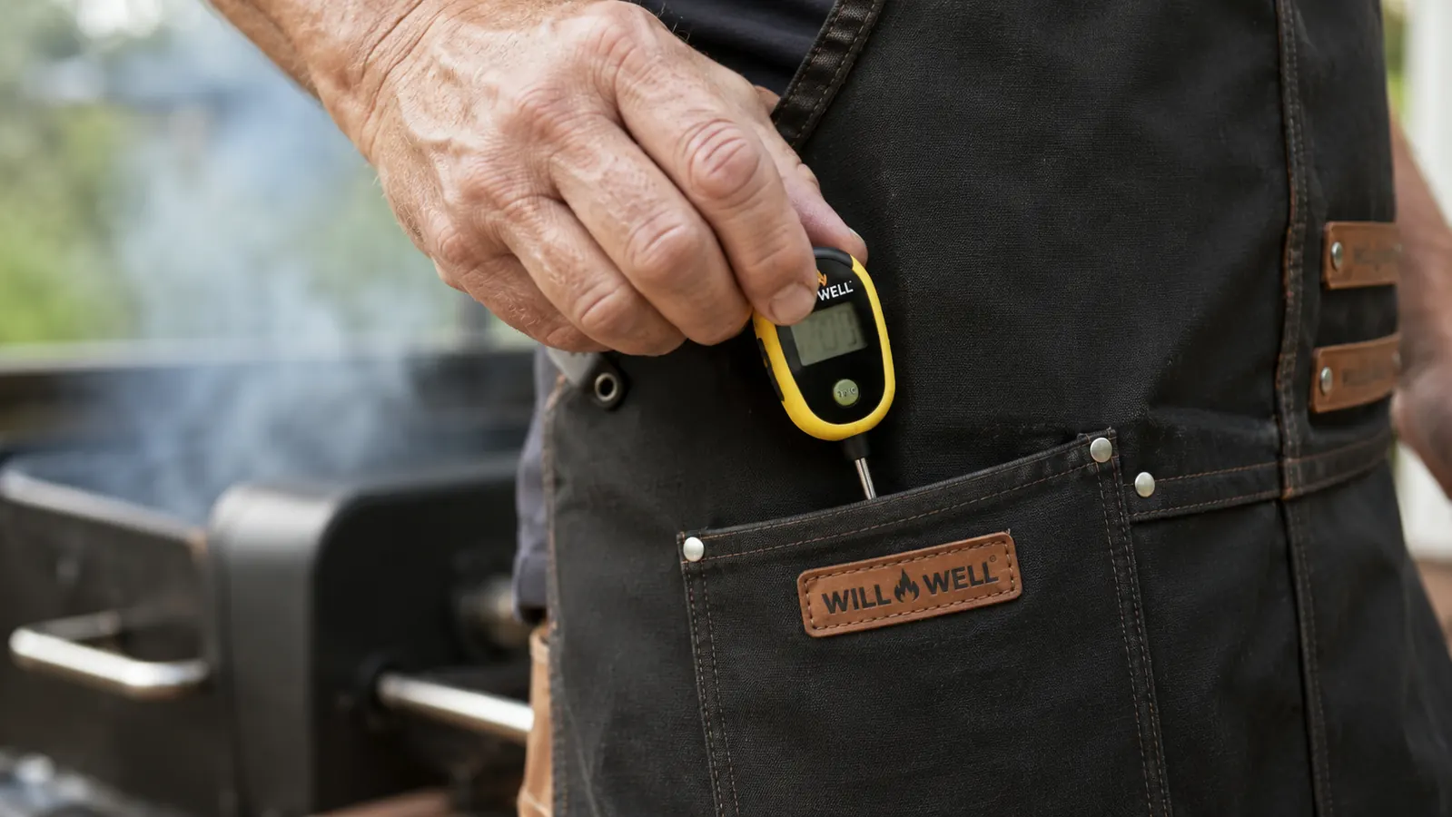 Close-up of a hand tucking an instant read thermometer into the front pocket of a black chef apron