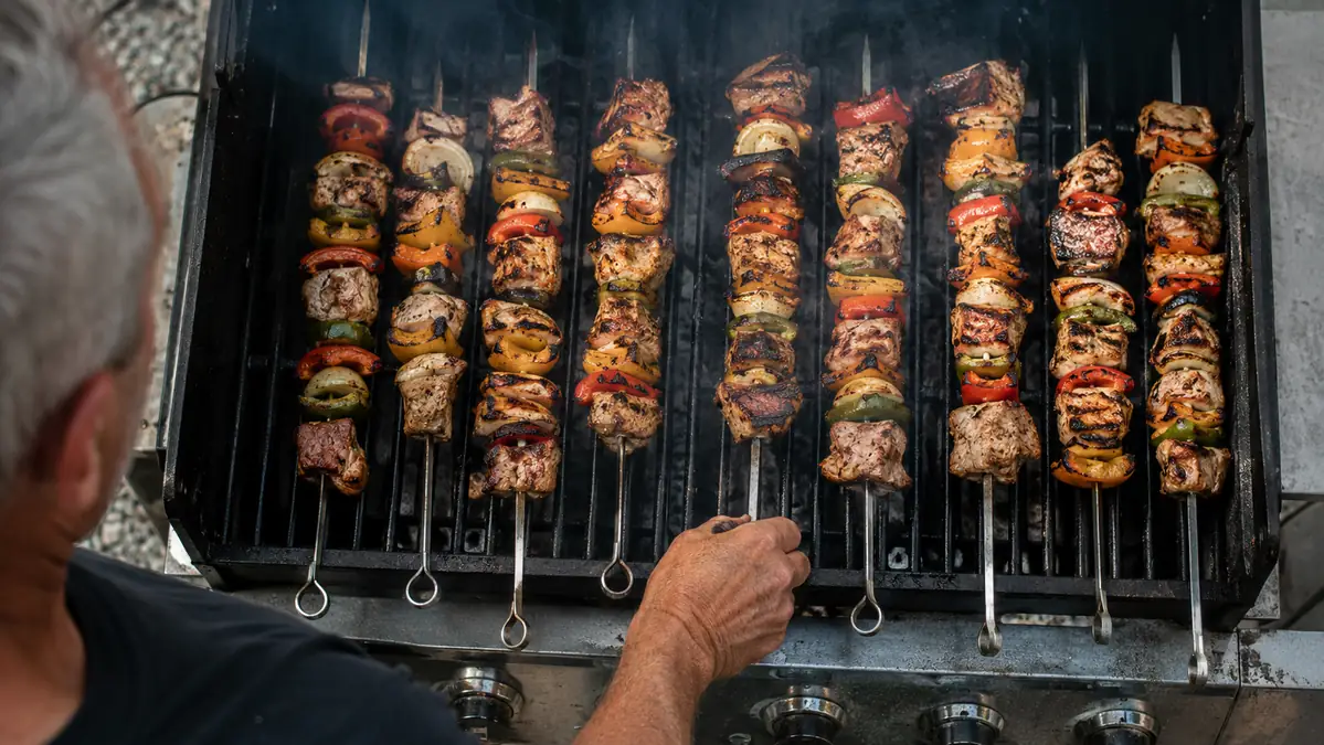 Kabobs lined up evenly on a hot grill grate, flat skewers resting flush without rolling