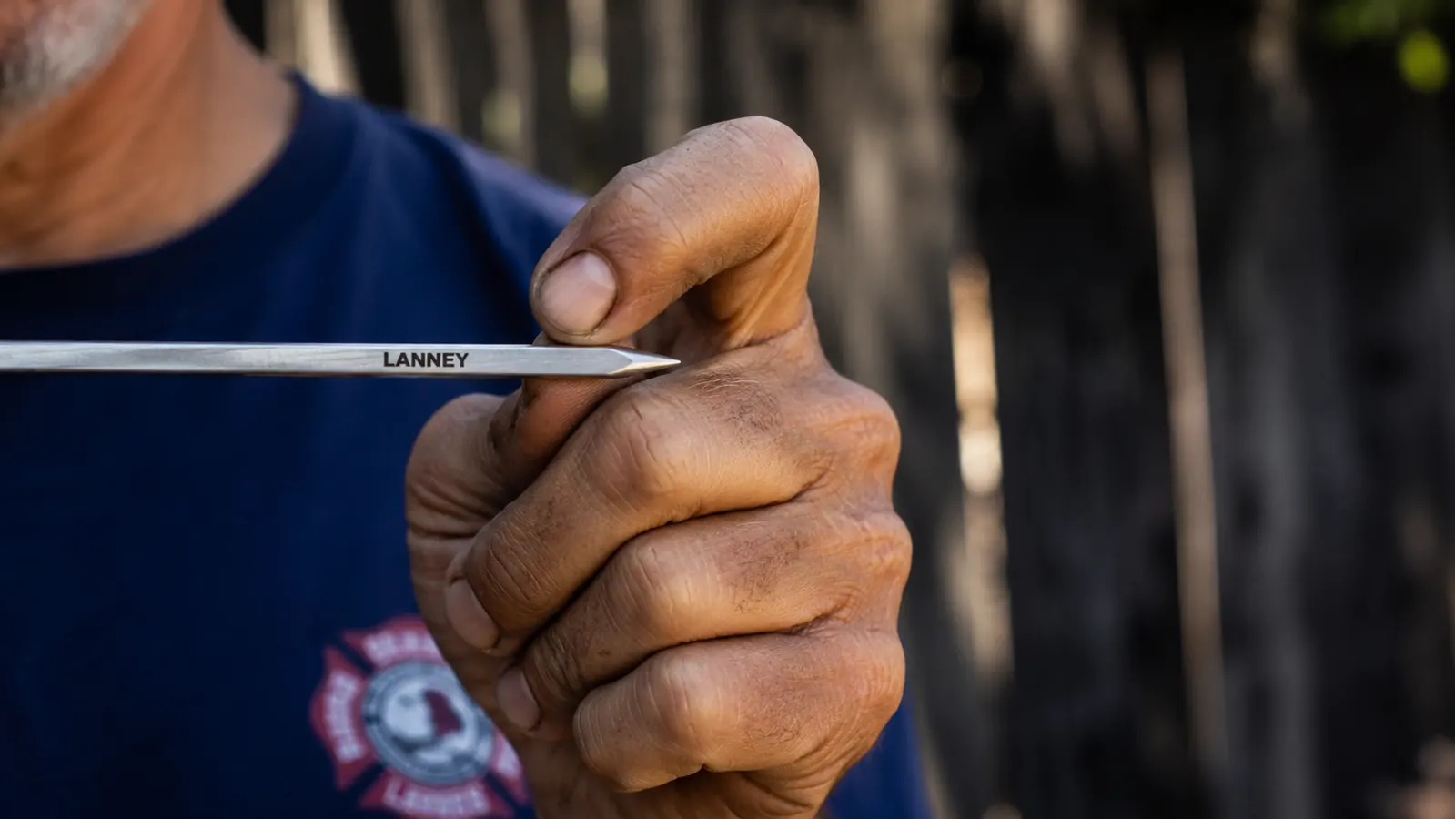 A close-up of a thumb pressed carefully against the sharp tip of a flat stainless steel skewer to test its point